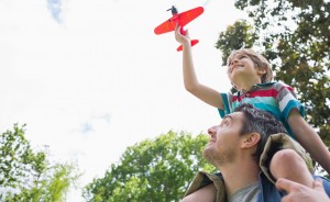 father and son playing with toy plane with son on father's shoulders